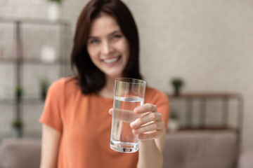 Close up blurred background of young woman stretch hand with glass of clear pure still mineral water, happy millennial girl recommend clean aqua for hydration, refreshment, healthy lifestyle concept