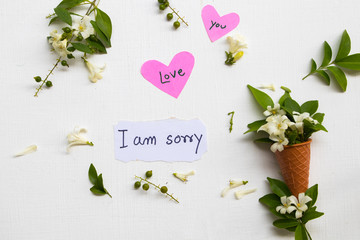 i am sorry ,i love you on pink paper hearts message card handwriting with jasmine flowers in cone arrangement flat lay style on background white 