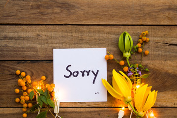 i am sorry message card handwriting with yellow flowers ylang ylang and light arrangement flat lay...