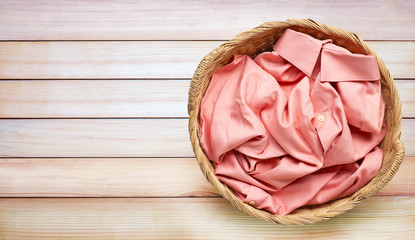 Colorful clothes in laundry basket on wooden background.