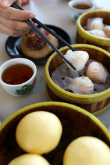 Close up hand picking up dim sum with chopsticks and enjoying variety of Chinese dim sum in the restaurant