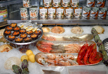 Fish shop counter with different seafood. Plates with big fresh tasty shrimps, sea urchin decorated with artichoke