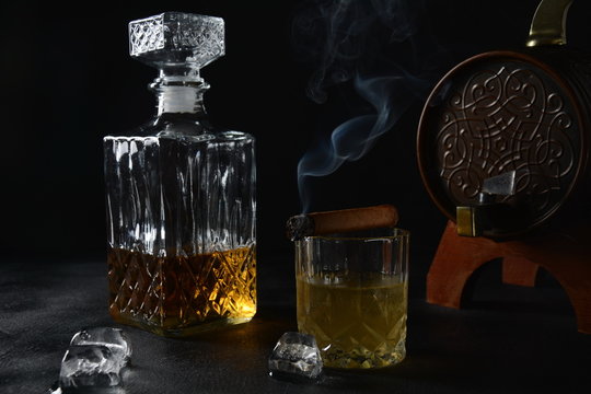 Glass of the whiskey with ice cubes and a square decanter, and cigar on a black  background.