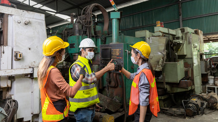 Factory in new normal. Foreman wearing face mask giving explanation to new trainees in a factory warehouse. Male supervisor giving instruction to his co-workers. Trainees give fist bump to supervisor