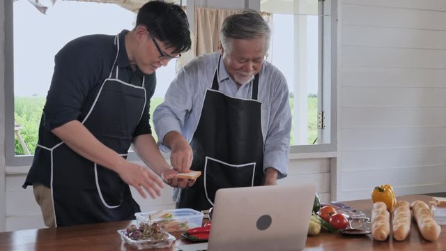 Senior father are enjoy cooking with adult son in the kitchen at home and using laptop.