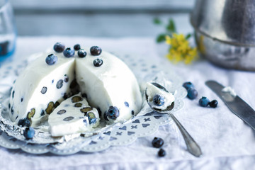 Obraz na płótnie Canvas Homemade tasty cold dessert of yogurt , blueberries and gelatin, decorated with raw berries in white tablecloth background with spoon ,cup, knife nearby, fresh, healthy food concept