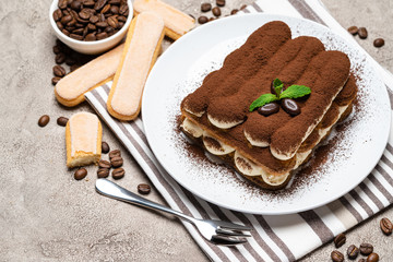 Classic tiramisu dessert and savoiardi cookies on ceramic plate on concrete background