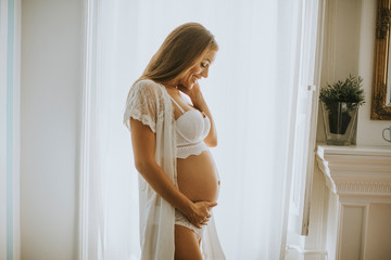Pretty young pregnant woman standing by the windowl in the room