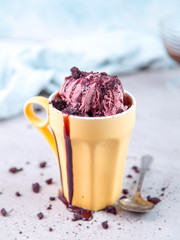 Cherry red ice cream in a regular yellow mug and spoon, on a blue background, with topping and crumbs. Unusual serve of dessert, copy space.
