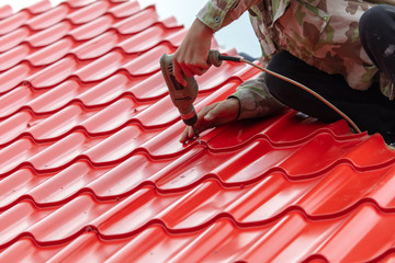 Workers install red metal tiles on the roof