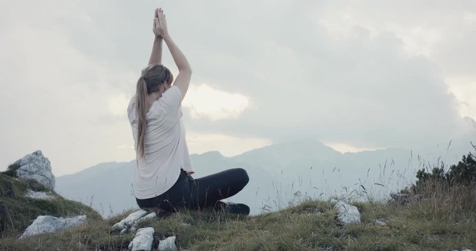 Young active woman doing yoga relaxation meditation to relax after hiking sit on rock hike on a fall or autumn cloudy evening