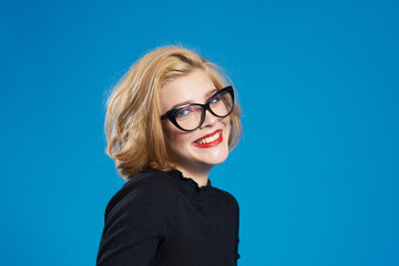 Fototapeta premium Blonde with short hair red lips glasses black jacket blue isolated background
