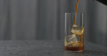 Obraz na płótnie Canvas pour coffee over ice cubes in glass to make iced coffee on terrazzo countertop