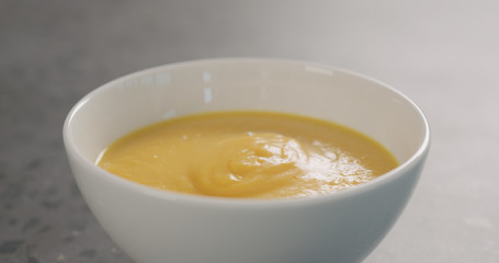 Pumpkin cream soup in white bowl on concrete background