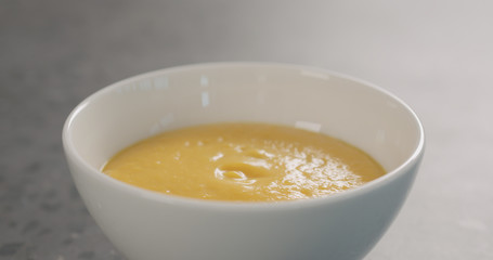 Pumpkin cream soup in white bowl on concrete background