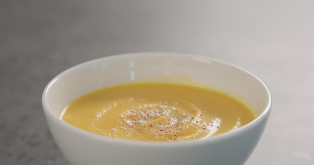 Pumpkin cream soup in white bowl on concrete background