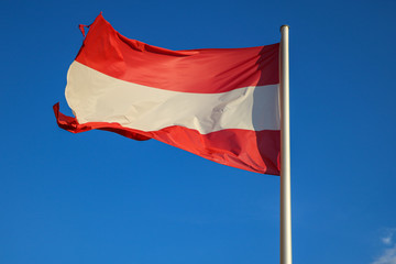 The Austrian flag flutters in the wind against the blue sky.