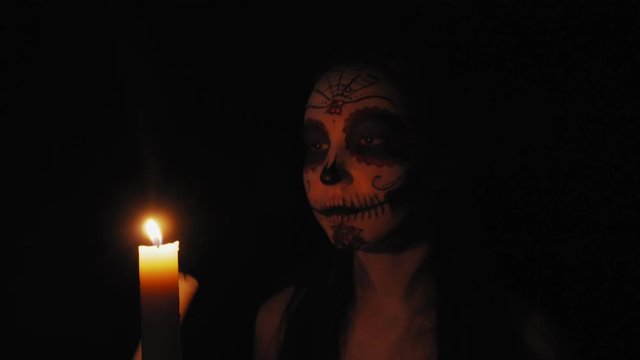 Portrait of a girl with Сatrina Calavera makeup. The girl in the dim light of the candle goes to the camera. High quality 4k footage