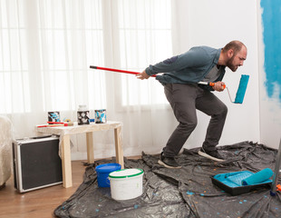 Man excitement during home repair singing at roller brush. Apartment redecoration and home...