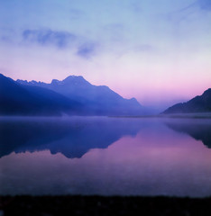 Fototapeta na wymiar A fisherman rowing among the fog on the lake of Silvaplana in the Engadin valley at sunrise with mountains reflecting in the water