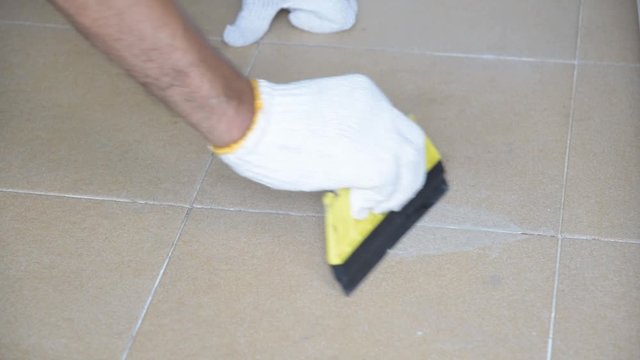 Construction worker in white gloves is working to grout the tiles in the bathroom.