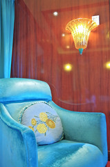 Turquoise velvet arm chair against wooden wall with lamp and curtain in suite stateroom or cabin on...