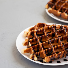Yummy Homemade Belgian Sugar Waffles on a white plate on a gray background, side view. Copy space.