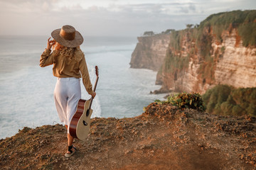 woman traveler hold the guitar standing on the cliff and looking for view of the sea and sunset on...