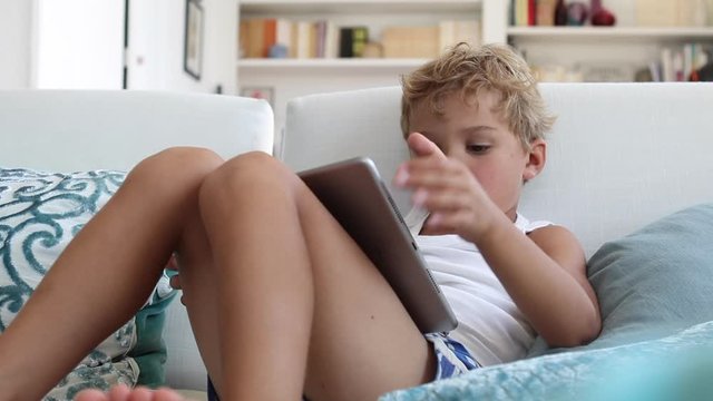 Cute toddler boy watching content online with tablet at home sofa