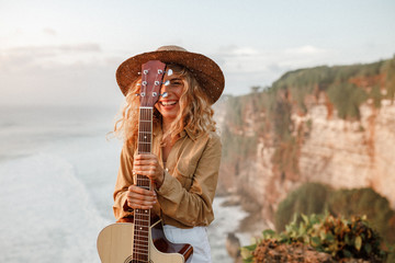 Face of a girl looking at the camra and smiling, eye is covered with the neck of the guitar. She...