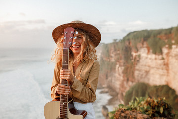 Face of a girl looking at the camra and smiling, eye is covered with the neck of the guitar. She was playing guitar near the sea at  sunny summer day.