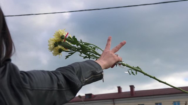 Close-up of the hand of a girl participating in an anti-government rally. The girl protests against the official election results and holds a bunch of flowers in her hand and shows a  victory hand. 