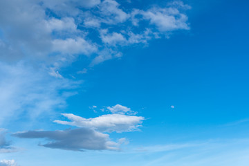 Blue sky with white cloud and visible moon in the daytime.