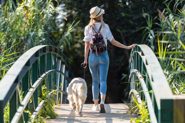 Attractive young amateur photograph woman walking with her dog crossing over a bridge in the park.