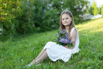 Naklejka na ściany i meble A little girl holds a bouquet of lilacs on a beautiful Sunny day. Cute girl outdoors in a blooming garden.