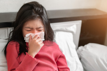Sick asian girl have hight fever flu and sneezing into tissue on bed in bedroom, Healthcare and prevent the spread infection virus concept, Selective focus.