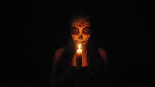 Portrait of a girl with Сatrina Calavera makeup. The girl in the dim light of the candle goes to the camera. High quality 4k footage