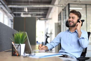 Smiling male business consultant with headphones sitting at modern office, video call looking at...