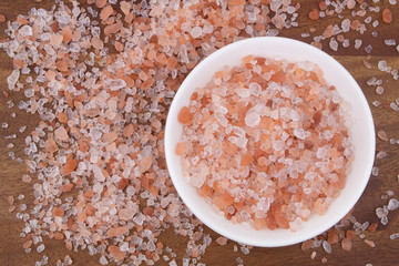 Himalayan pink salt in bowl and on wooden table, top view	