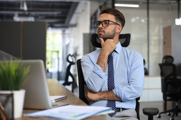 Obraz premium Focused businessman thinking at modern office into report file calculating stock market earnings, startup business.