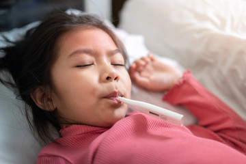 Asian girl with digital thermometer in her mouth on bed at morning time, Sick child with high fever  Selective focus, Healthy and infection concept