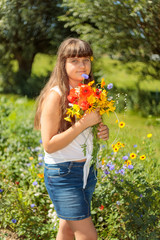 A young beautiful girl holding a summer flowers flower, bright green nature background