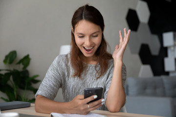 Excited millennial Caucasian female look at smartphone screen triumph get pleasant good text message, overjoyed young woman feel euphoric winning online lottery on cellphone gadget, luck concept
