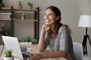Happy young Caucasian red-haired woman sit at desk distracted form computer work look in distance...