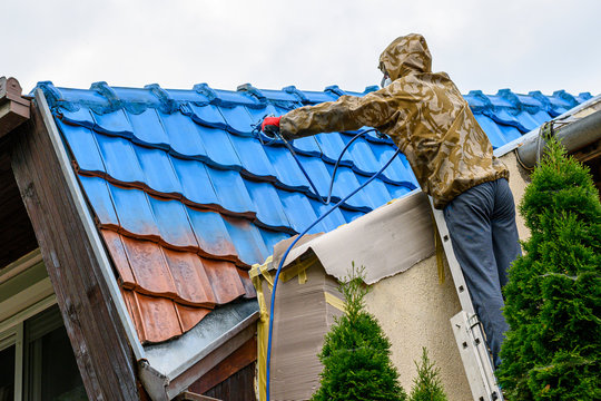 Professional painting old roof in blue color diligently. Work at heights.