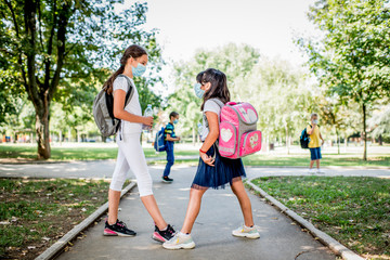 Two school girl greets by touching feet. Greeting during pandemic. .