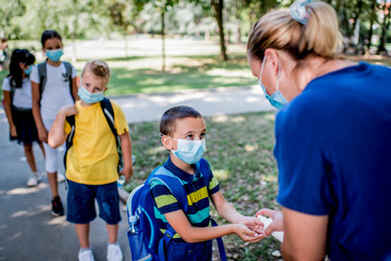 Woman sanitizing school children's hands outdoors