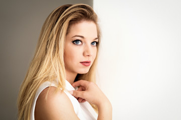 Fototapeta premium Attraktive junge Frau mit blauen Augen in weissem Kleid steht am Fenster