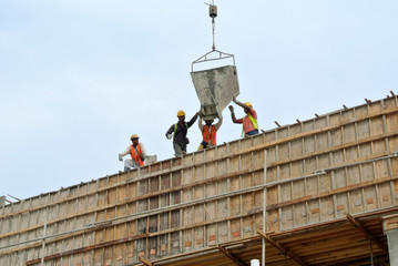 Naklejka premium JOHOR, MALAYSIA -MAY 06, 2016: A group of construction workers pouring concrete using concrete bucket into the column formwork at the construction site. 