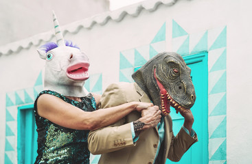 Crazy senior couple wearing unicorn and t-rex mask while dancing outdoor - Mature trendy people...
